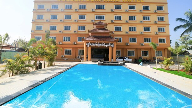 A hotel with a swimming pool in front, a multi-story building, and palm trees around.