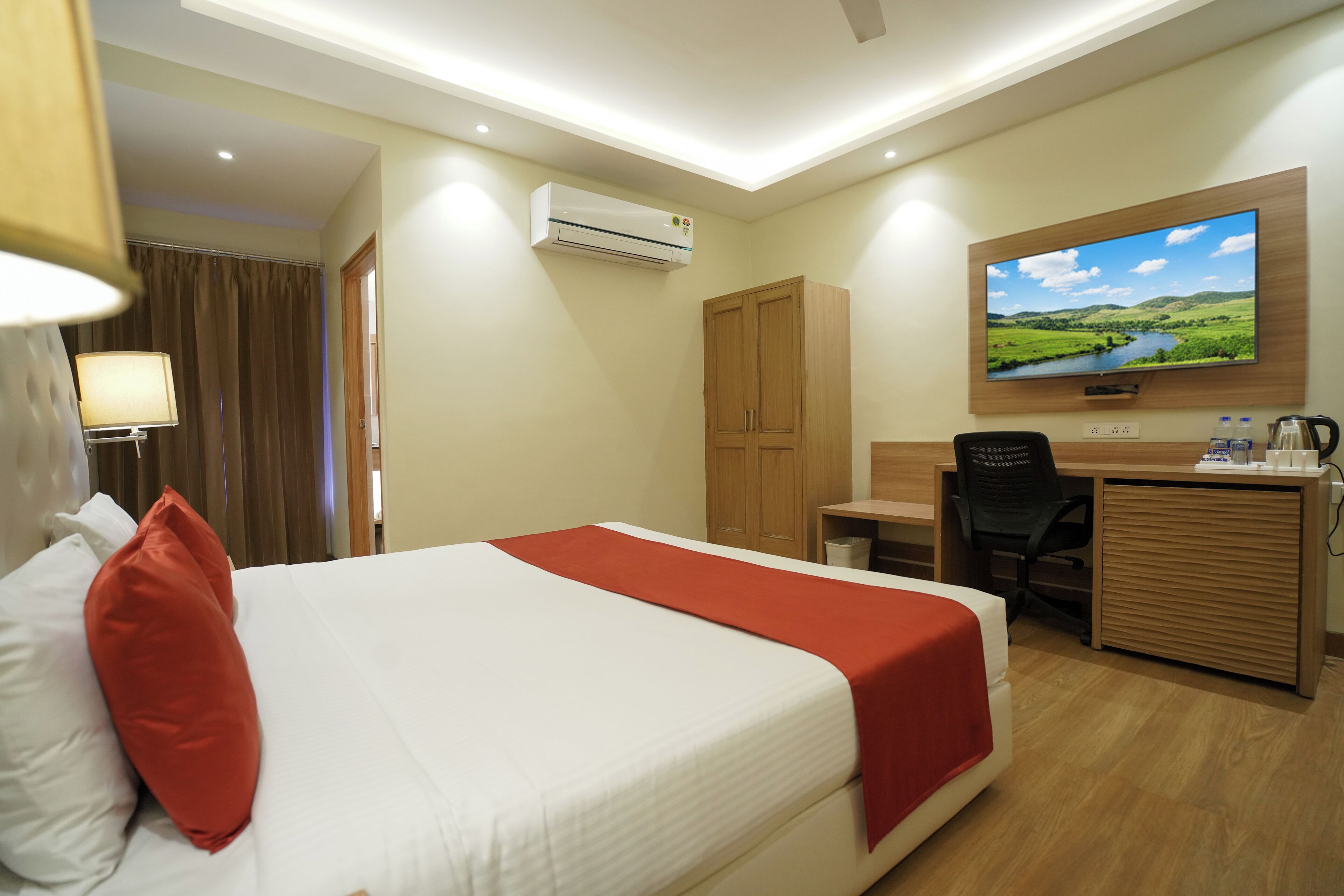 Una habitación de hotel con cama, escritorio, silla, televisor y aire acondicionado.
