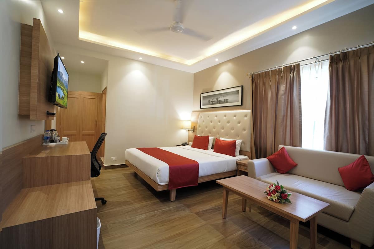 A hotel room with a bed, a sofa, a desk, and a TV mounted on the wall.