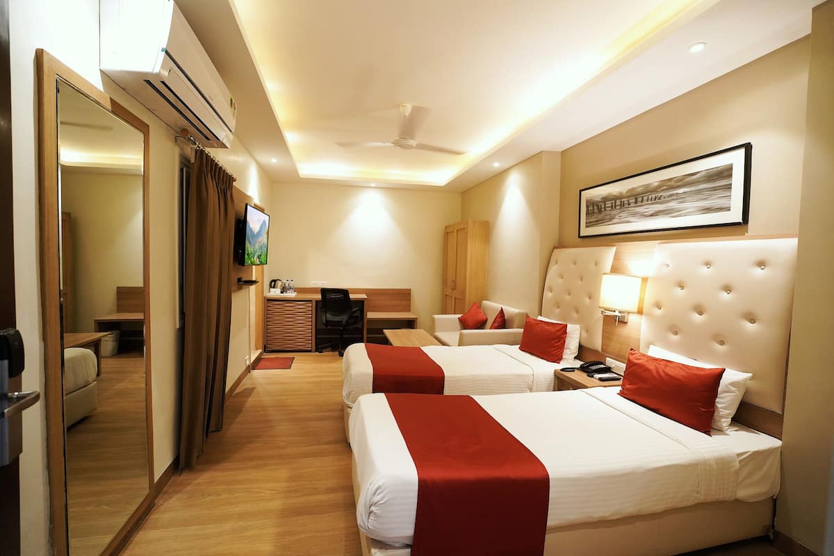 A hotel room with two beds, a desk, a chair, a television, and a ceiling fan.