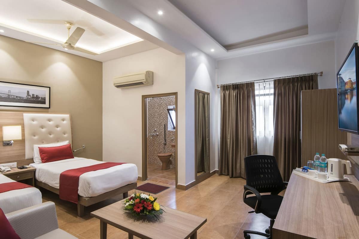 A hotel room with two beds, a desk, a chair, a TV, and a bathroom visible through a door.