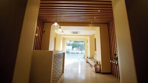 Un moderno vestíbulo de hotel con un área de estar central, una pared con diseño y un techo con listones de madera horizontales.
