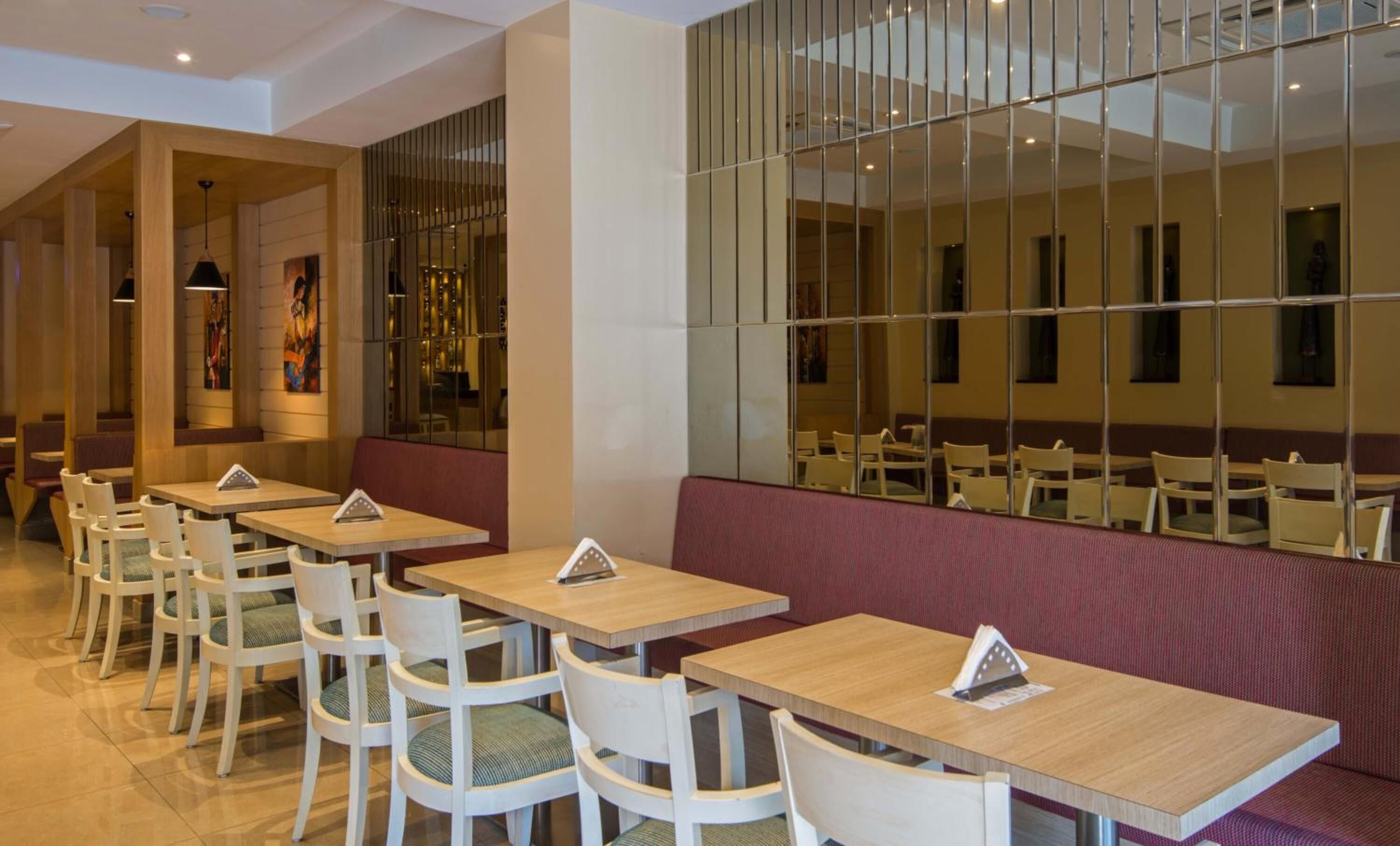 Un restaurant doté de nombreuses tables et de banquettes, de chaises en bois et d’un grand mur recouvert de miroirs.