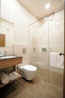 Een moderne badkamer met een glazen douchecabine, een houten wastafelmeubel, een wit toilet en een handdoekrek.