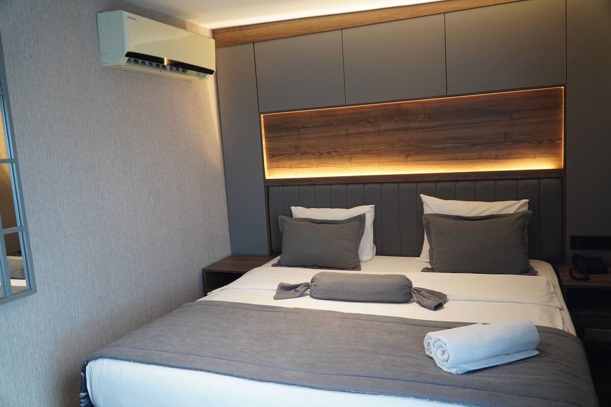A modern hotel room with a neatly made bed, a wooden headboard, and a wall-mounted air conditioner.