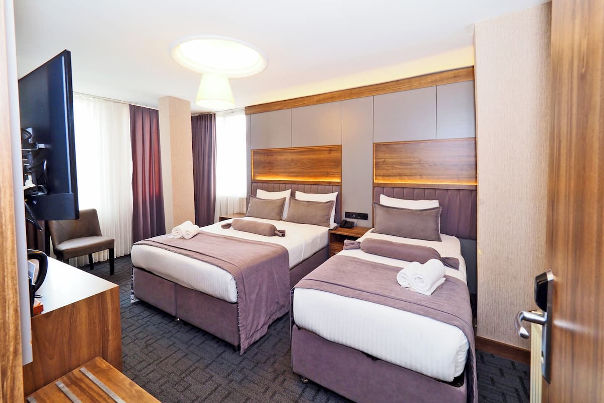 A hotel room with two beds, a TV, a desk, and a large window.