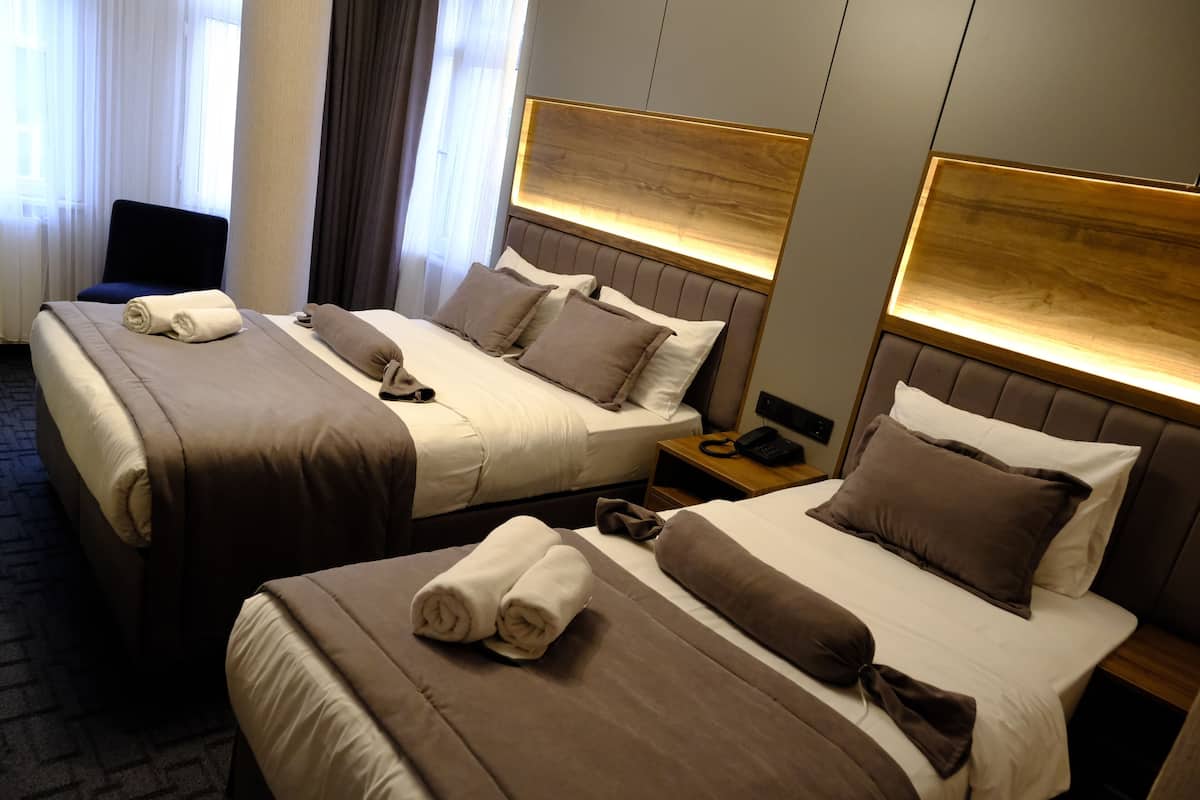 A hotel room with two beds, each with a headboard, a bedside table with a phone, and a chair.