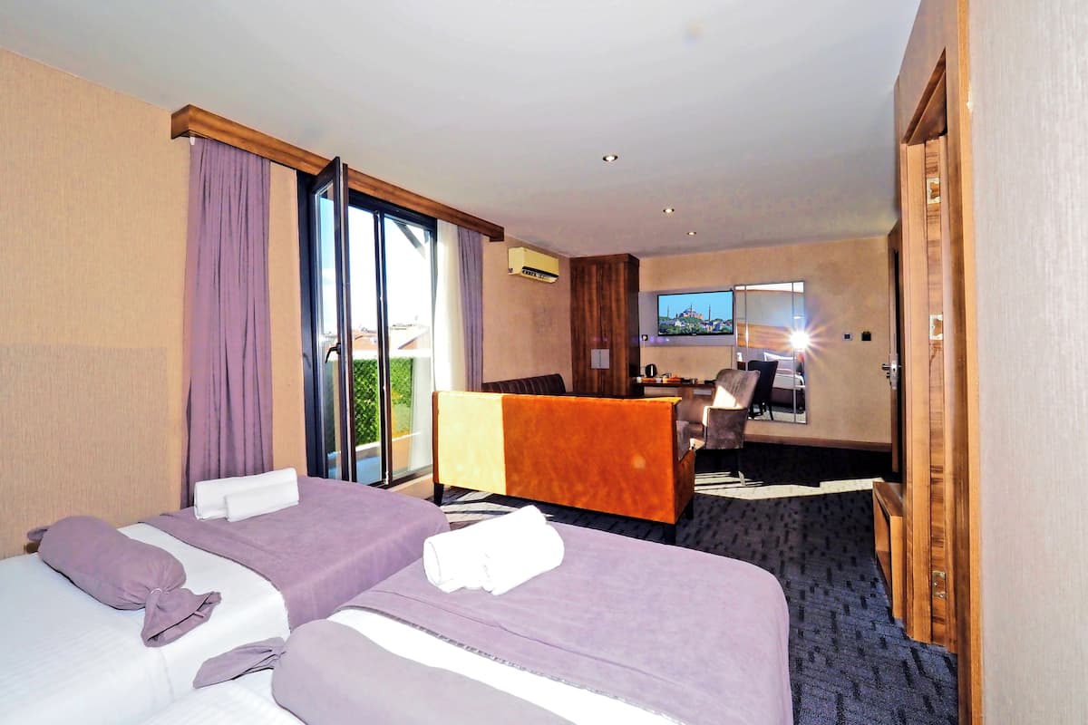 A hotel room with two beds, a desk, a TV, and a balcony with a view.