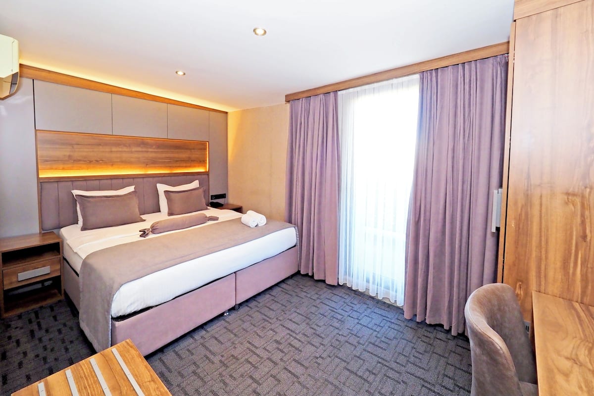 A hotel room with a large bed, a wooden headboard, a nightstand, a desk, and a chair.