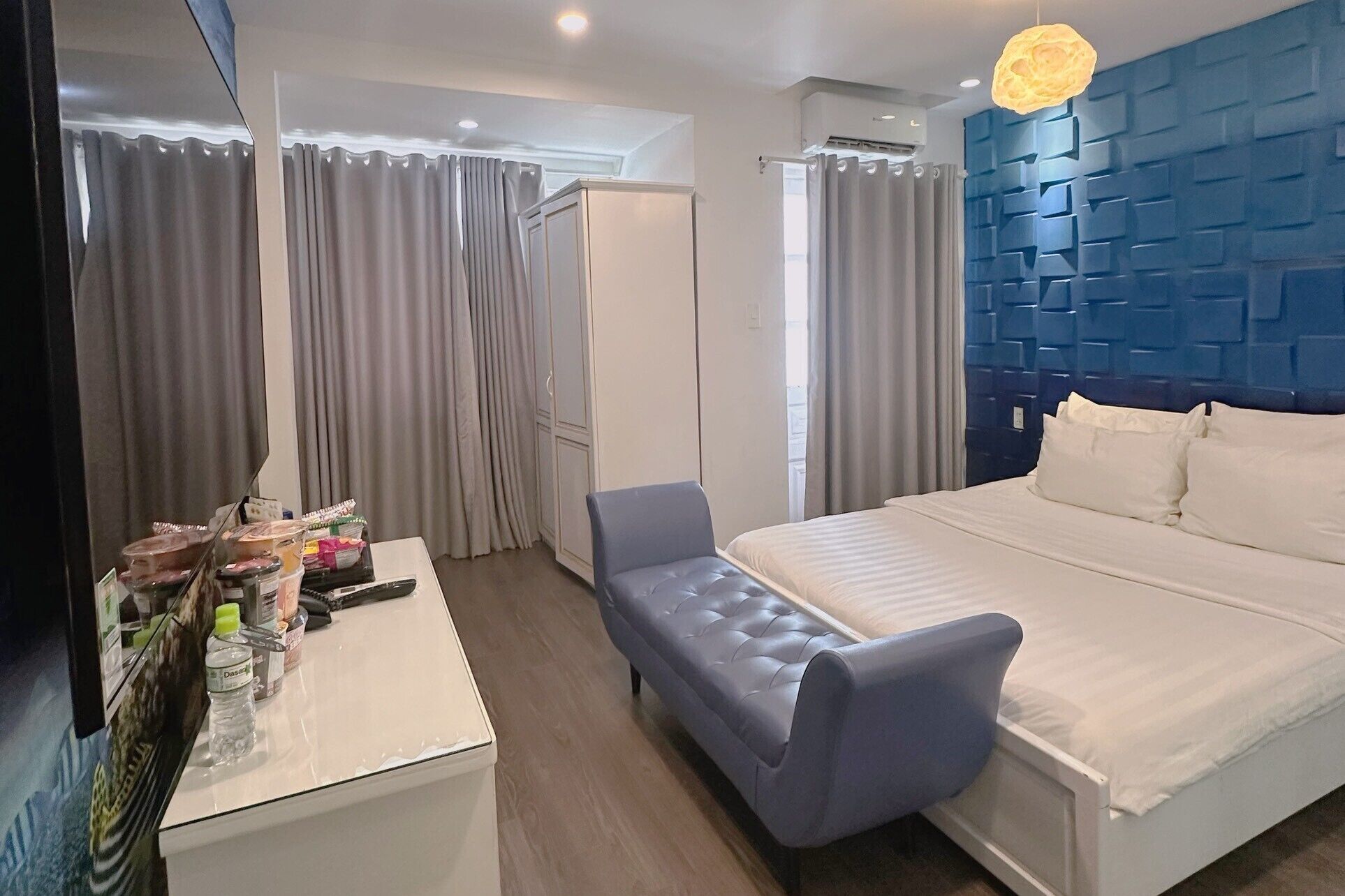 A hotel room with a bed, a chair, a desk with toiletries, and a blue accent wall.