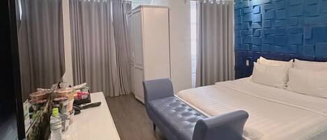 A hotel room with a bed, a chair, a desk with toiletries, and a blue accent wall.