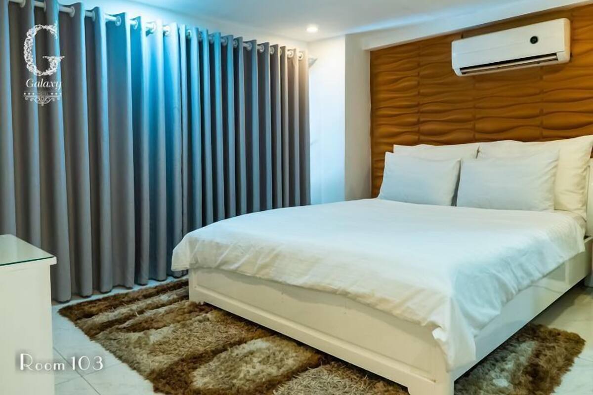 Een hotelkamer met een bed, gordijnen, een airconditioner en een vloerkleed.