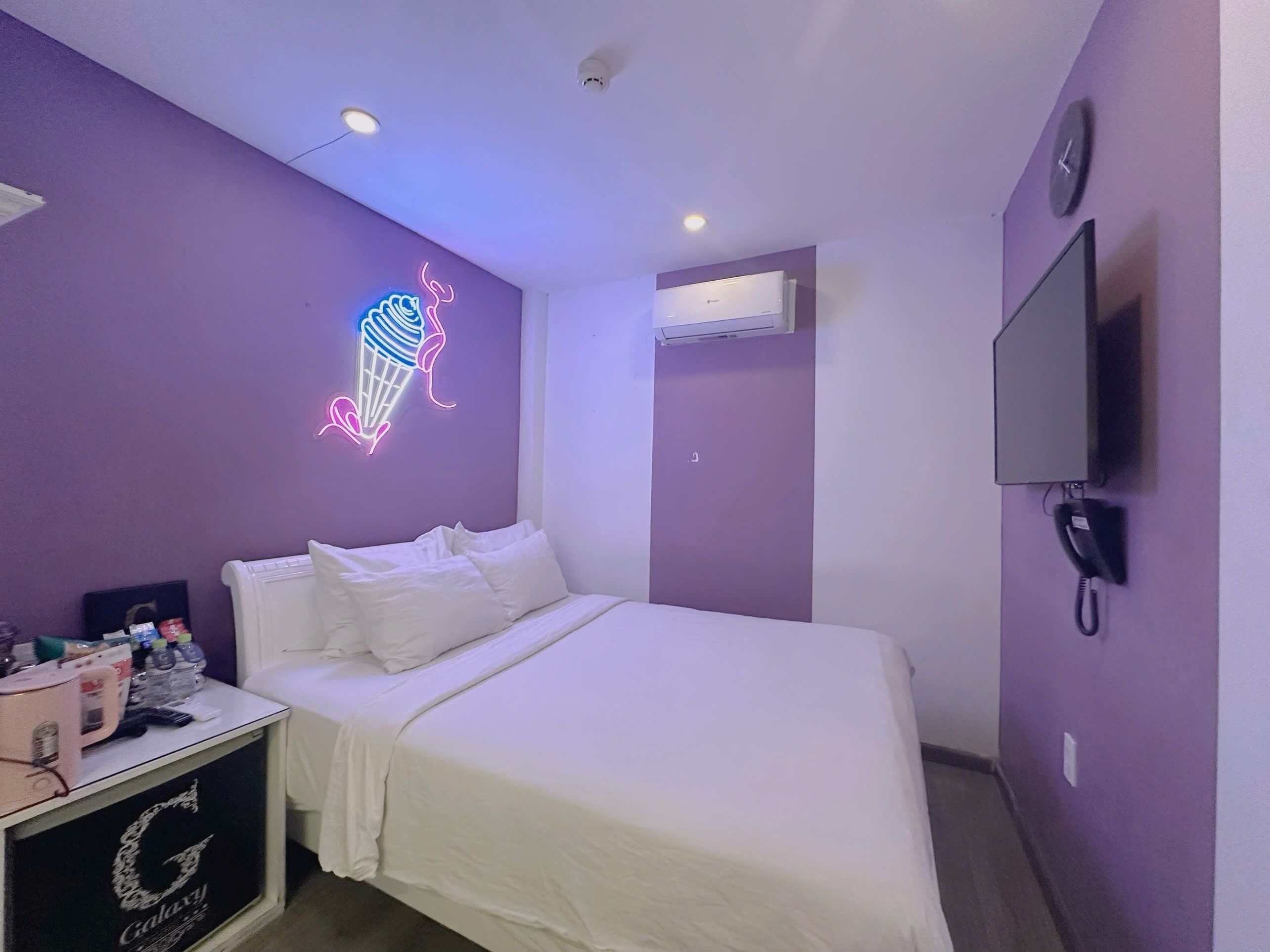 Habitación de hotel con una cama, un letrero de helado de neón, aire acondicionado, televisor y teléfono.
