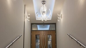 A modern staircase with a wooden door and glass panels, leading to a room with a chandelier.