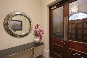 Een receptiegedeelte met een ronde spiegel, een vaas met bloemen en een houten deur.