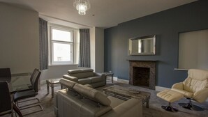 A modern living room with a fireplace, leather sofas, a glass coffee table, and a dining area with a glass table and chairs.