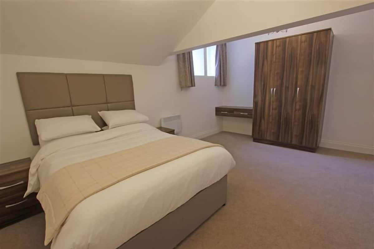 A bedroom with a large bed, a wardrobe, and a small bedside table.