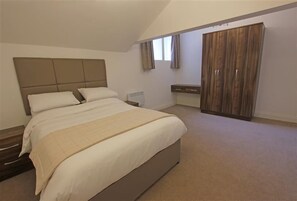 A bedroom with a large bed, a wardrobe, and a small bedside table.