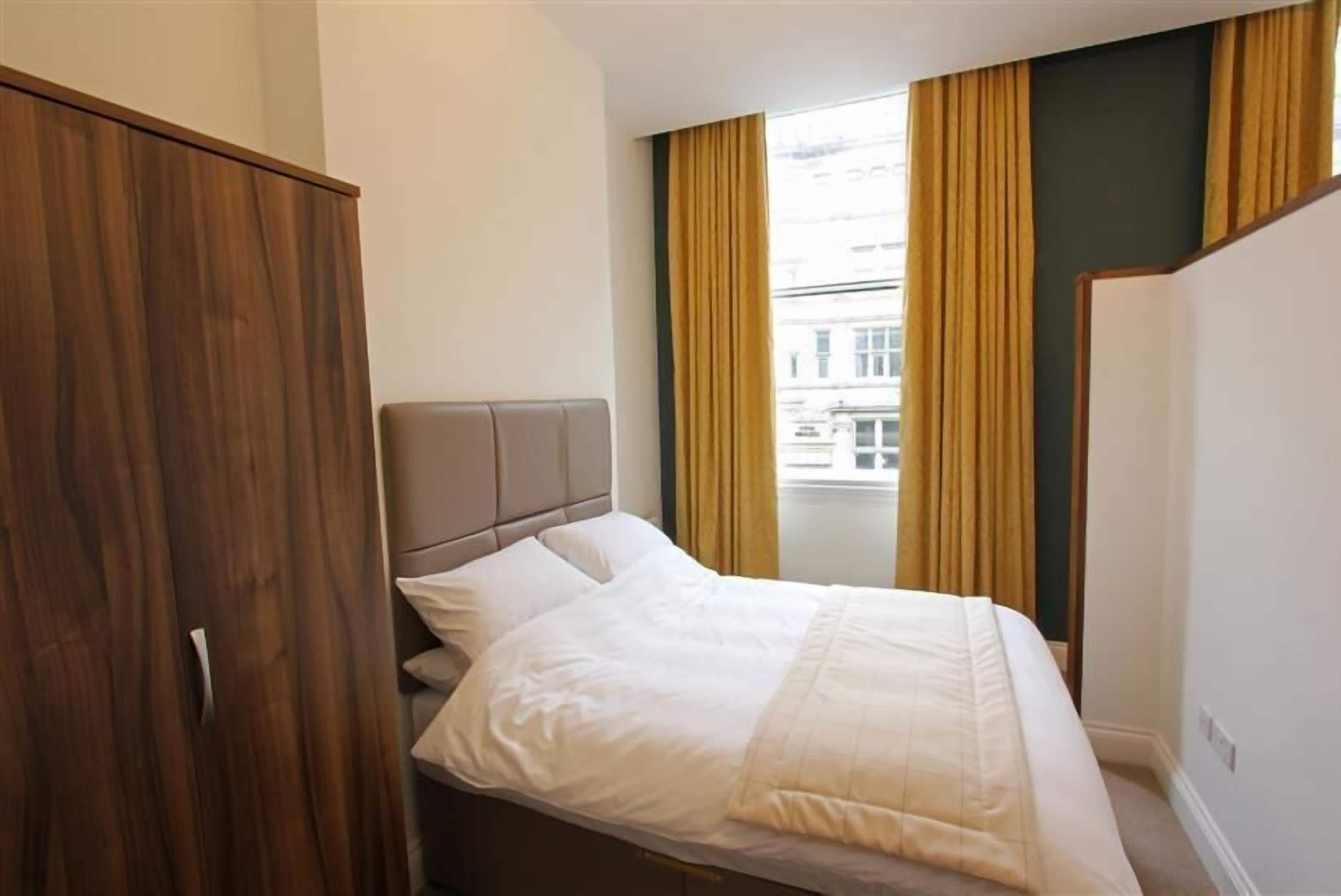 A bedroom with a bed, a wardrobe, and a window with curtains.