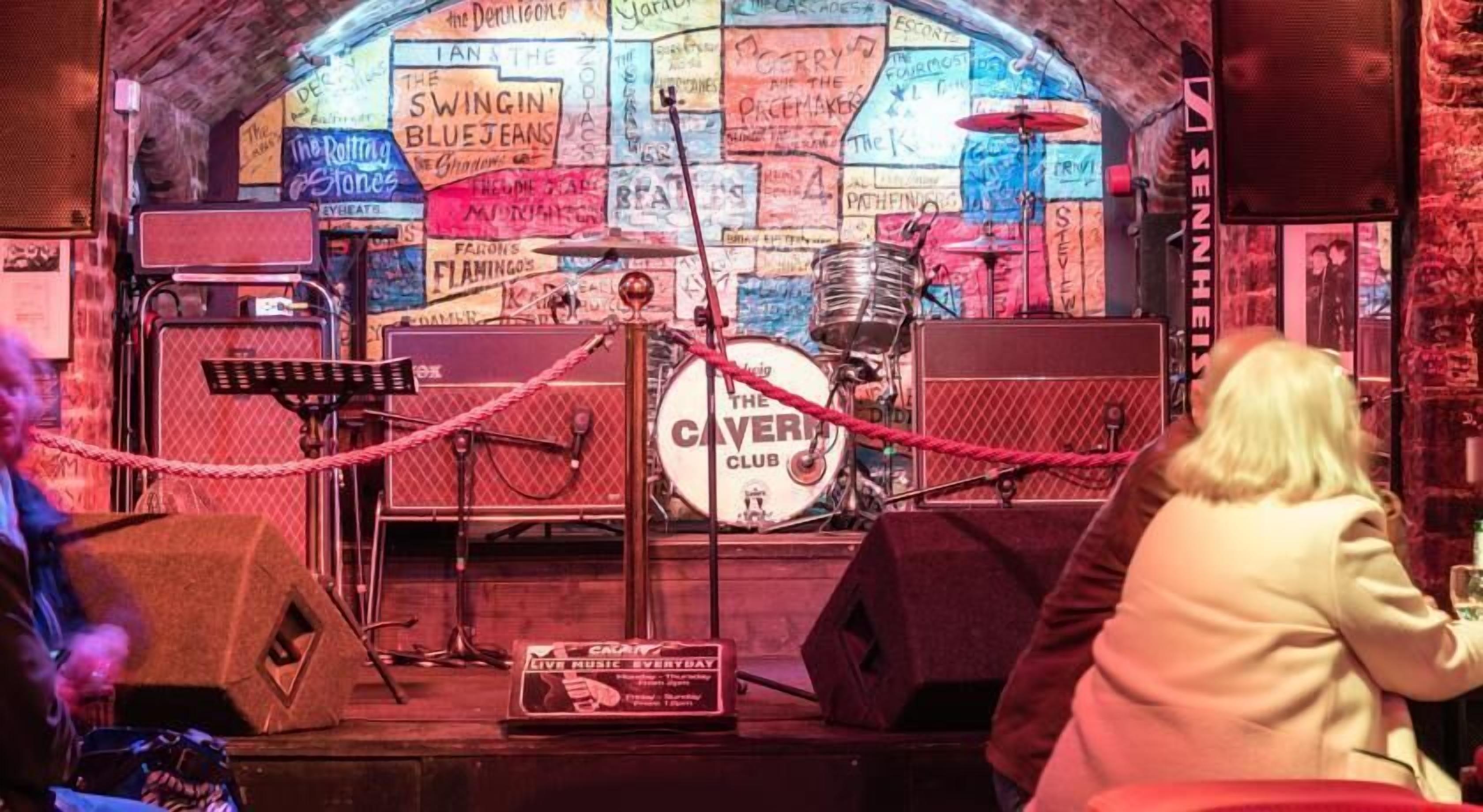 A music venue with a stage, drum set, and vintage posters on the walls.