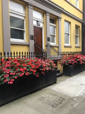 A yellow building with a black iron fence and red flowers in planters. - The Castle Collection 3 Union Court (Liverpool)