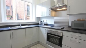 Una cocina moderna con armarios blancos, un horno de acero inoxidable, un microondas y una ventana que ofrece vistas a un edificio de ladrillo.