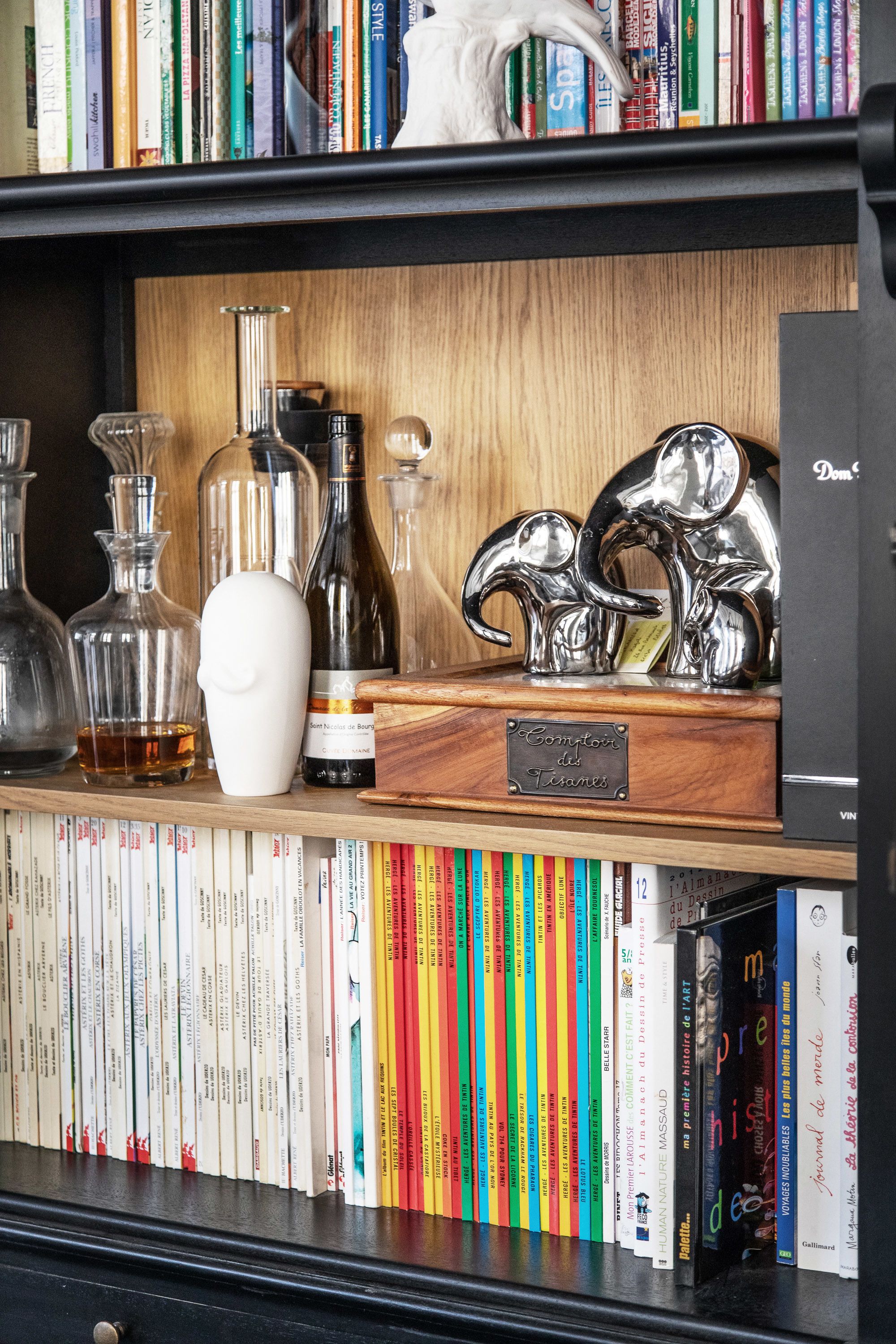 Een boekenplank met boeken, decoratieve flessen en een zilveren sculptuur.