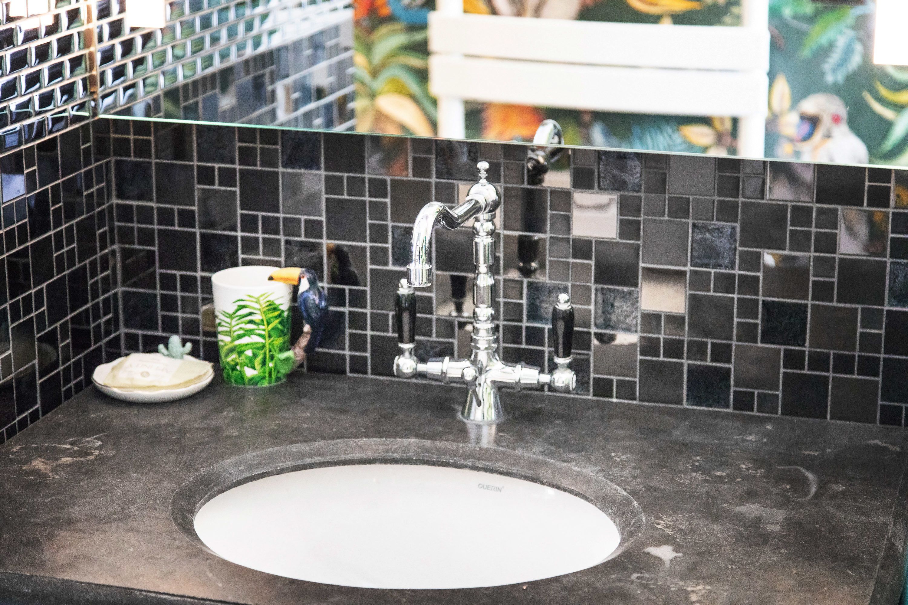 A bathroom sink with a modern faucet, a green plant in a cup, and a white plate on the counter.