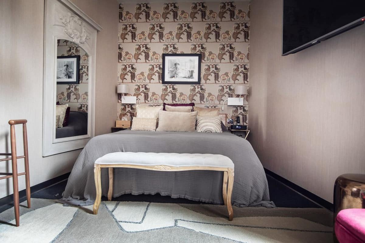 Une chambre à coucher comprenant un lit, des lampes de chevet, un banc, un miroir et un téléviseur.
