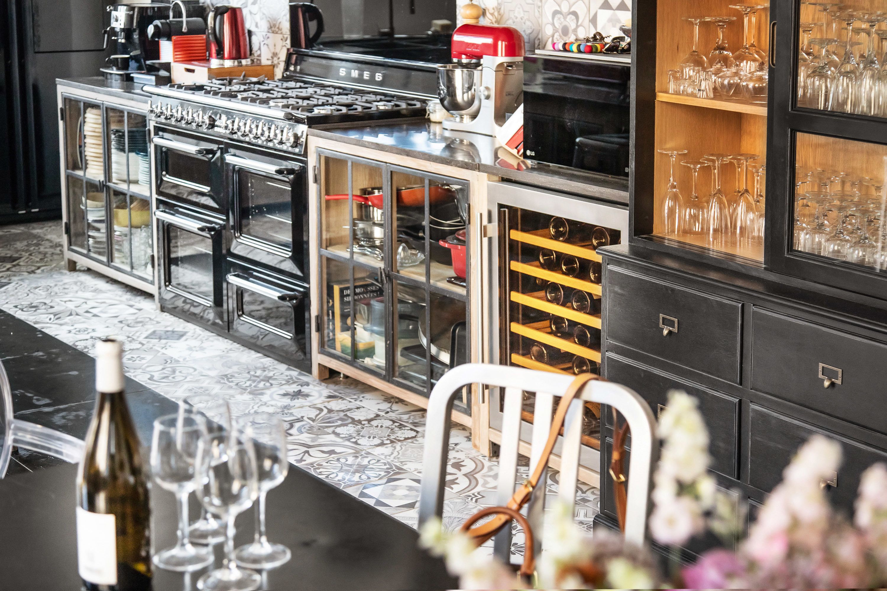 A kitchen with a stove, oven, and various kitchen appliances. There is a wine rack and a cabinet with glass doors.
