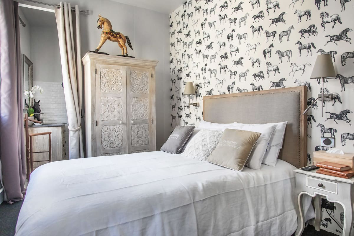 Une chambre bien rangée, avec un lit, une armoire en bois et un mur décoré d’un motif équestre.