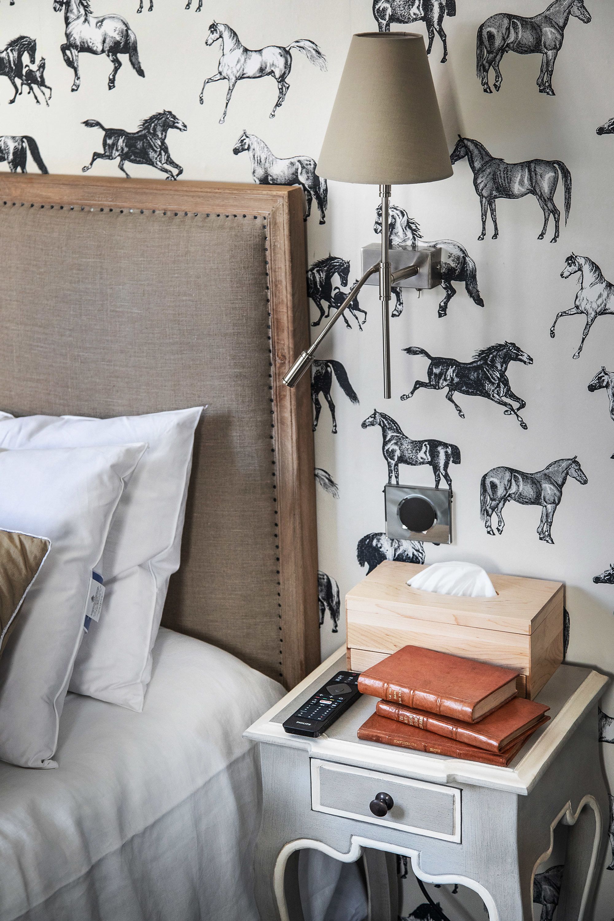 Ein ordentlich gemachtes Bett mit Kissen, ein Nachttisch mit Lampe, Radio und Büchern.