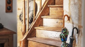 Una escalera de madera con barandilla, una estatua y un paraguas apoyado en la pared.