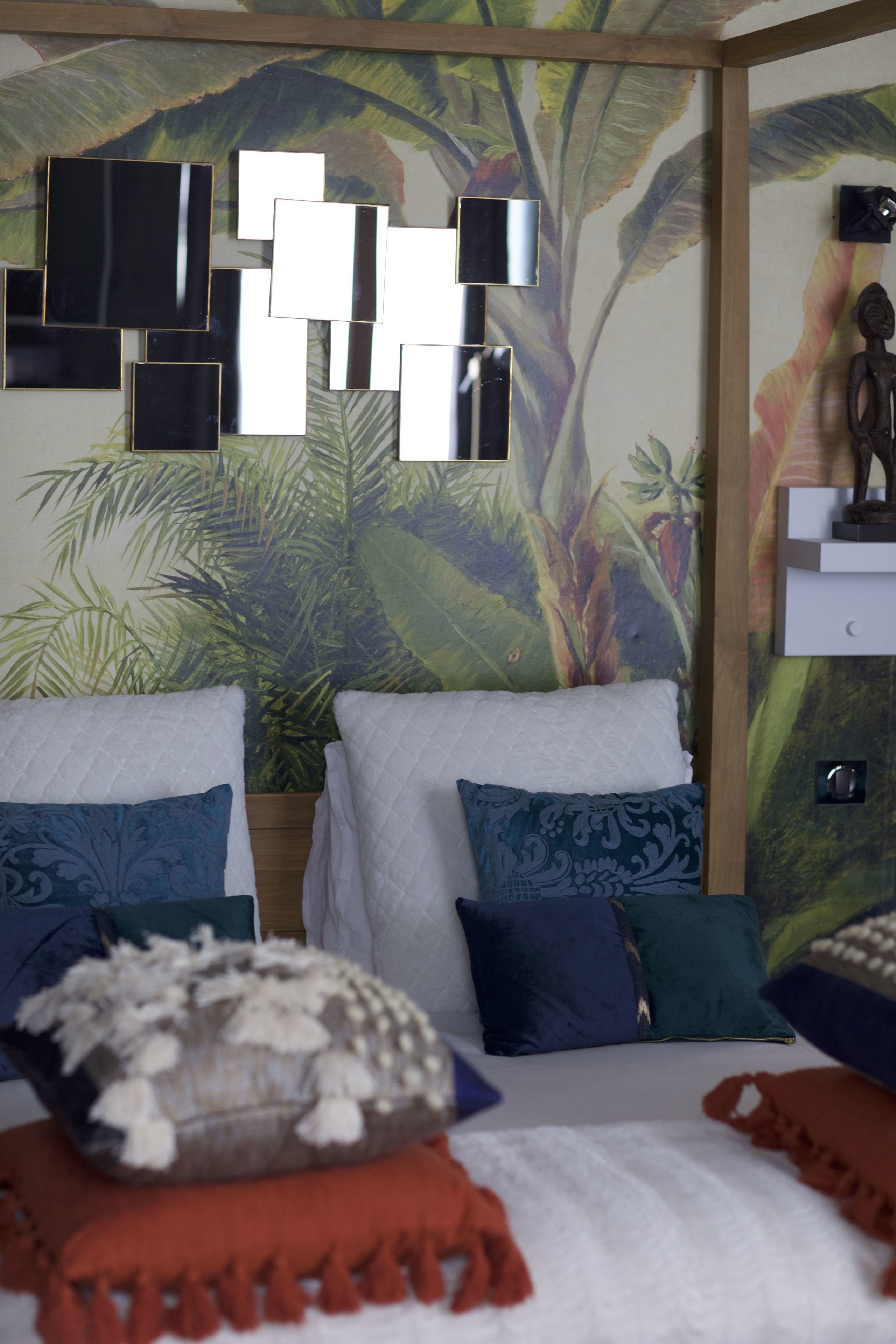 Un dormitorio con una cama grande, dos almohadas, una colcha y una pared con un mural tropical.