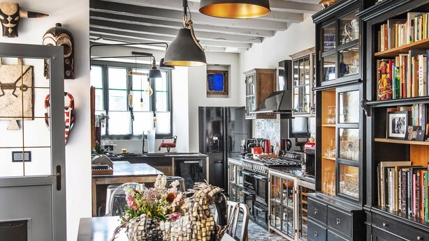 Una cocina moderna con armarios negros, una mesa de comedor con sillas y una lámpara colgante.