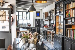 A modern kitchen with black cabinetry, a dining table with chairs, and a hanging pendant light. - La Bellême Bleue (Belleme)