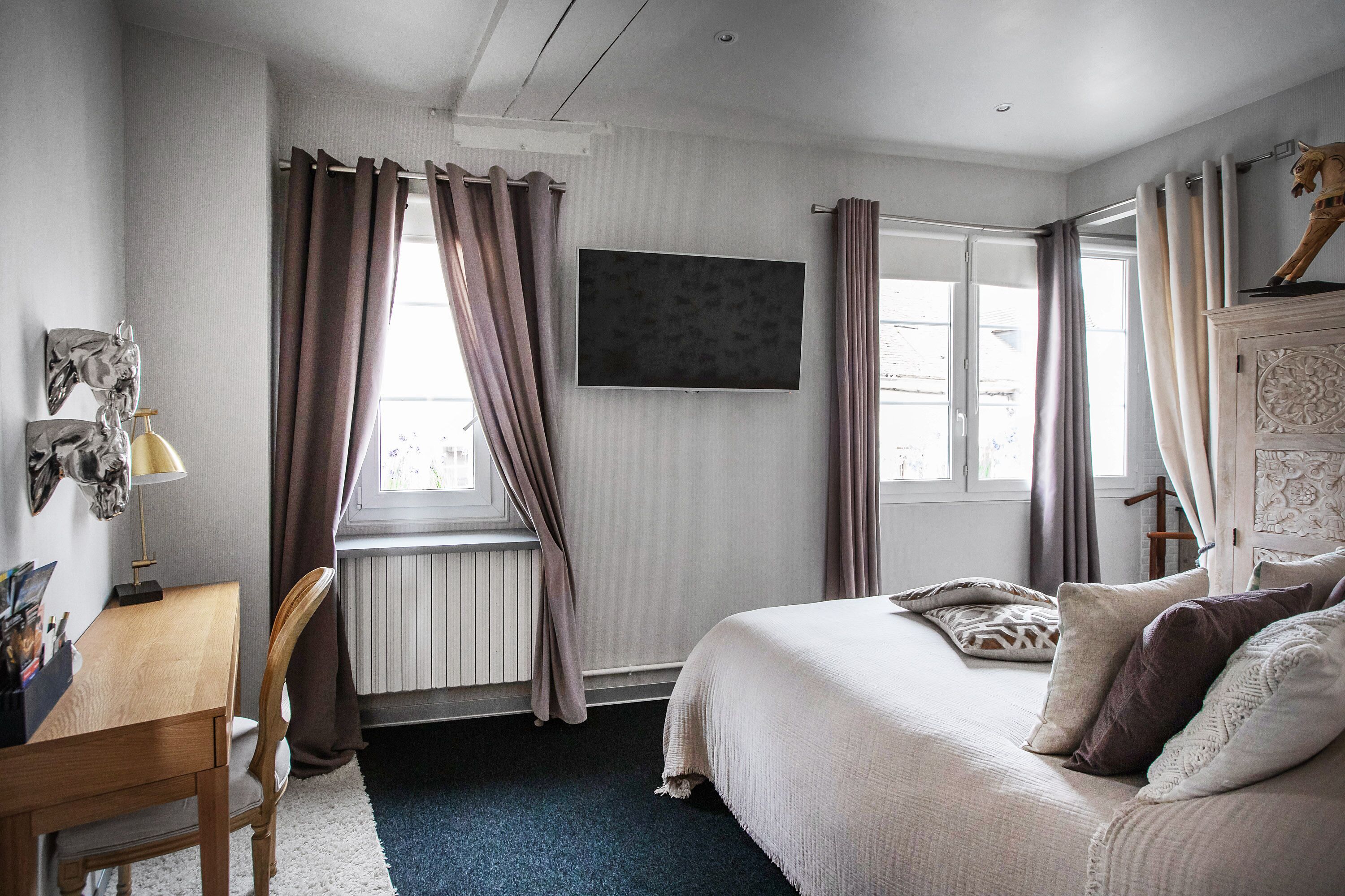 A bedroom with a bed, a desk, and a window with curtains.