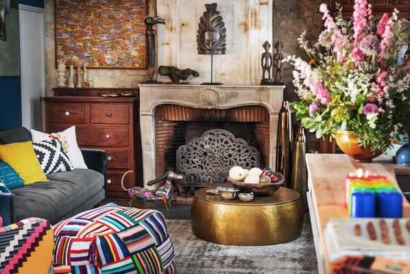Una sala de estar acogedora con chimenea, un sofá, cojines de colores y un cuenco decorativo sobre una mesa redonda.