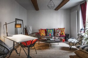 A cozy living room with a wooden table, a sofa with colorful cushions, a patterned armchair, and a hanging light fixture. - La Bellême Bleue (Belleme)