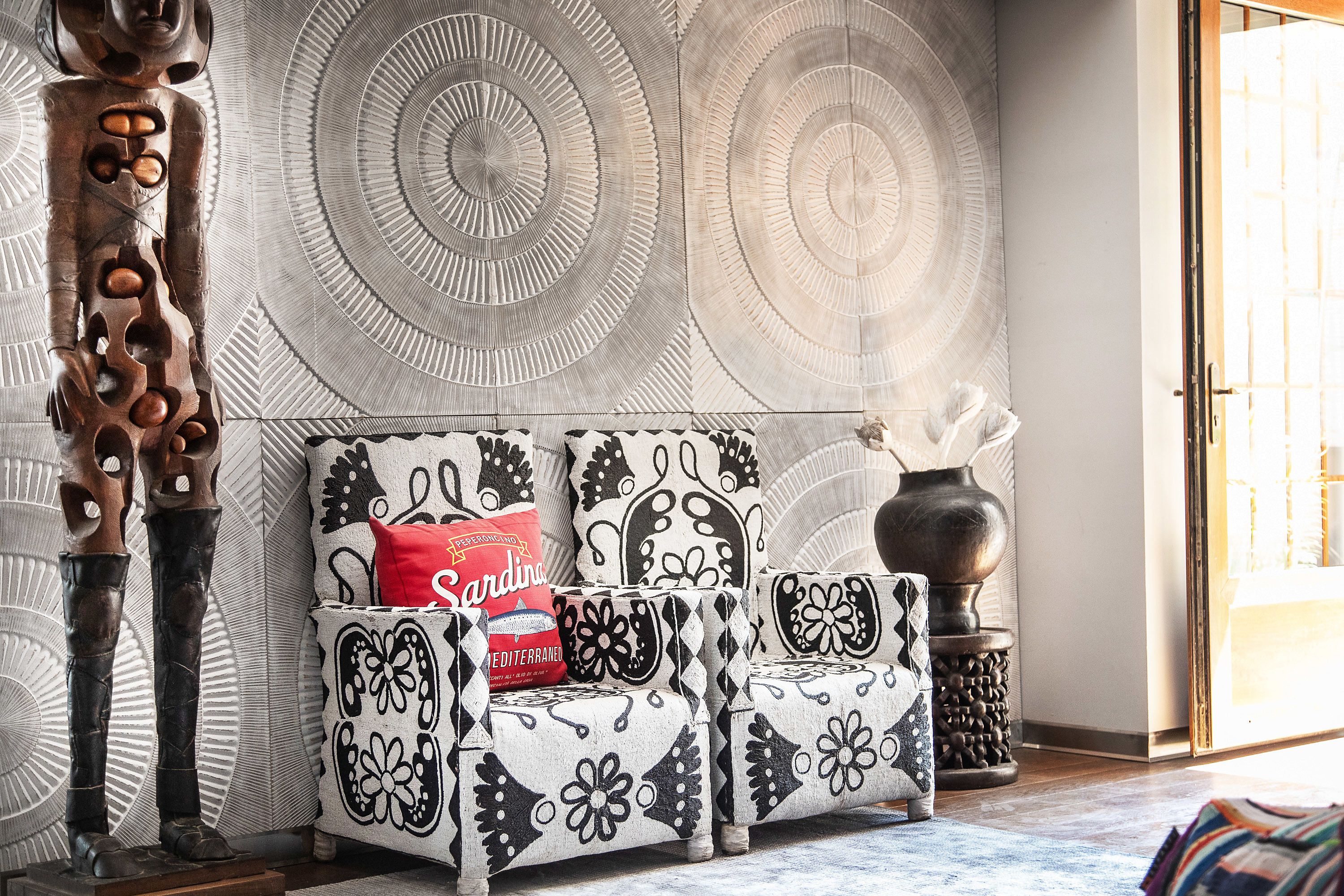 A living room with a patterned wall, a sofa with a red pillow, and a decorative vase.