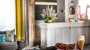 Una sala moderna con un sofá gris, cojines coloridos, un aparador de madera y un jarrón con flores.
