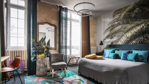 Un dormitorio con cama, una silla, una mesita y un ventanal grande.