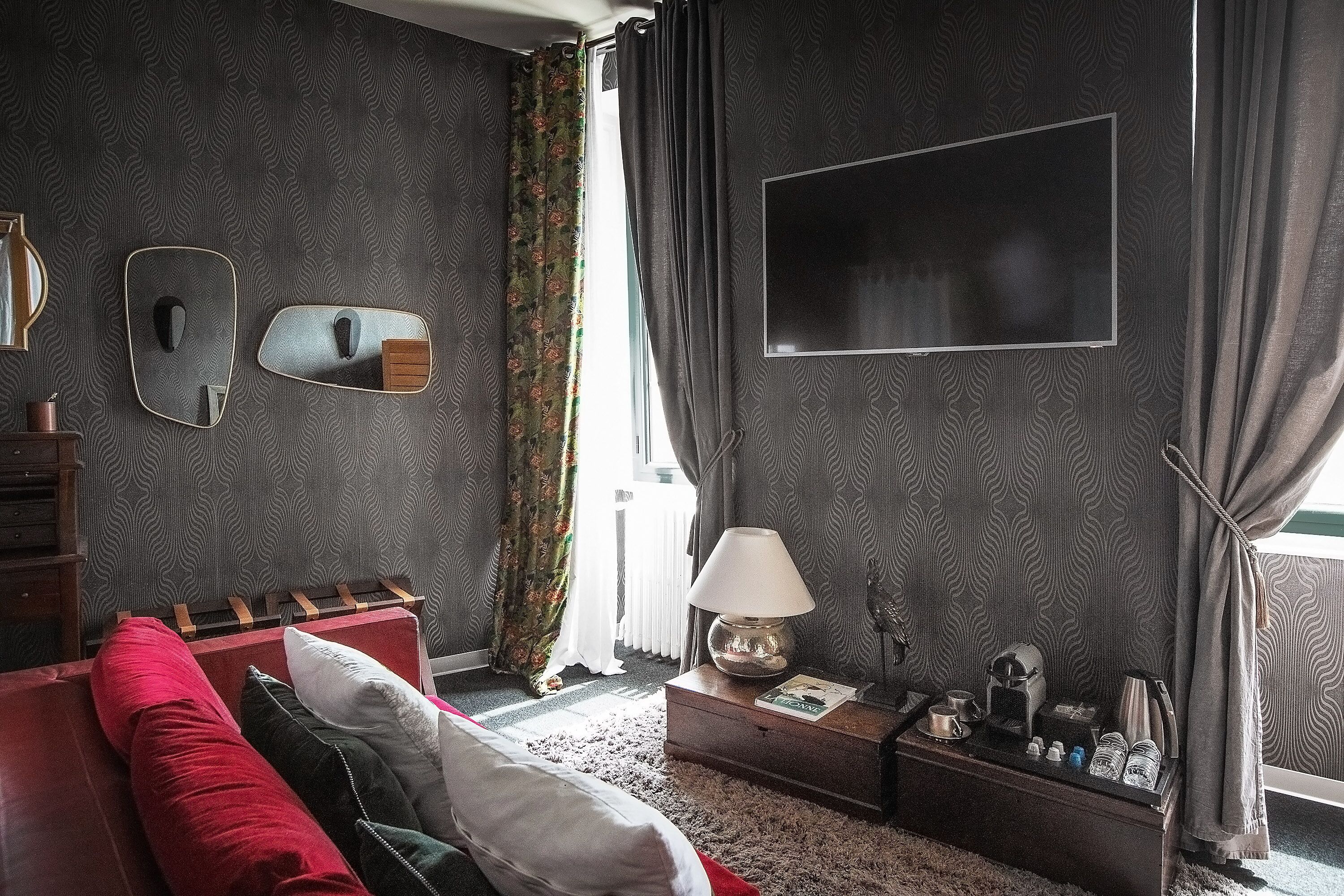 A room with a red sofa, a wooden side table with a lamp, a mirror, and a flat-screen TV mounted on the wall.