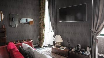 A room with a red sofa, a wooden side table with a lamp, a mirror, and a flat-screen TV mounted on the wall.