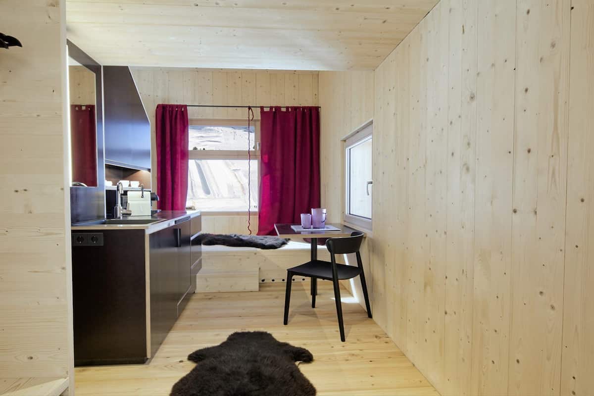 A compact kitchen with a sink, stove, and dining area with a chair and table.