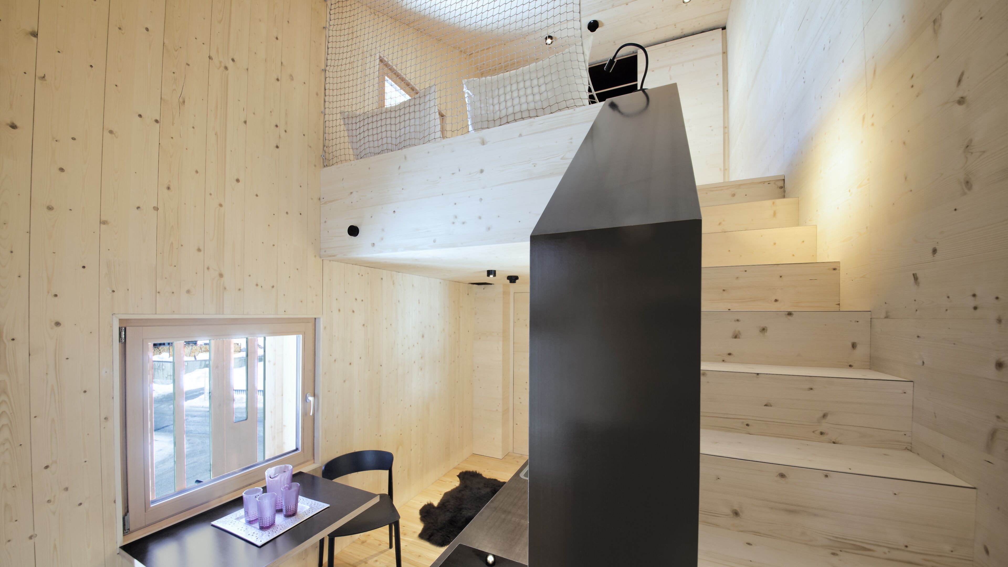 Un intérieur en bois comprenant un coin repas, une chaise noire, une table avec des tasses et une grande structure noire.