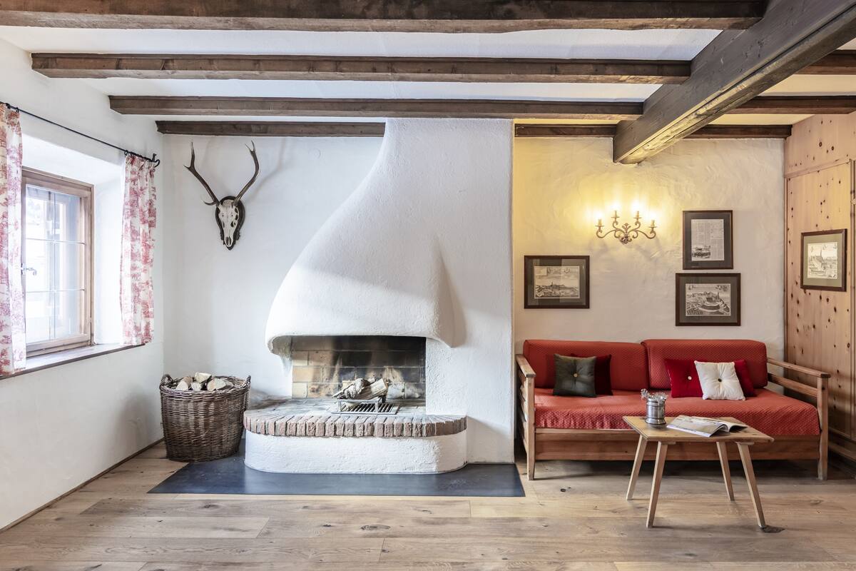 A cozy room with a fireplace, a red sofa, and wooden beams on the ceiling.
