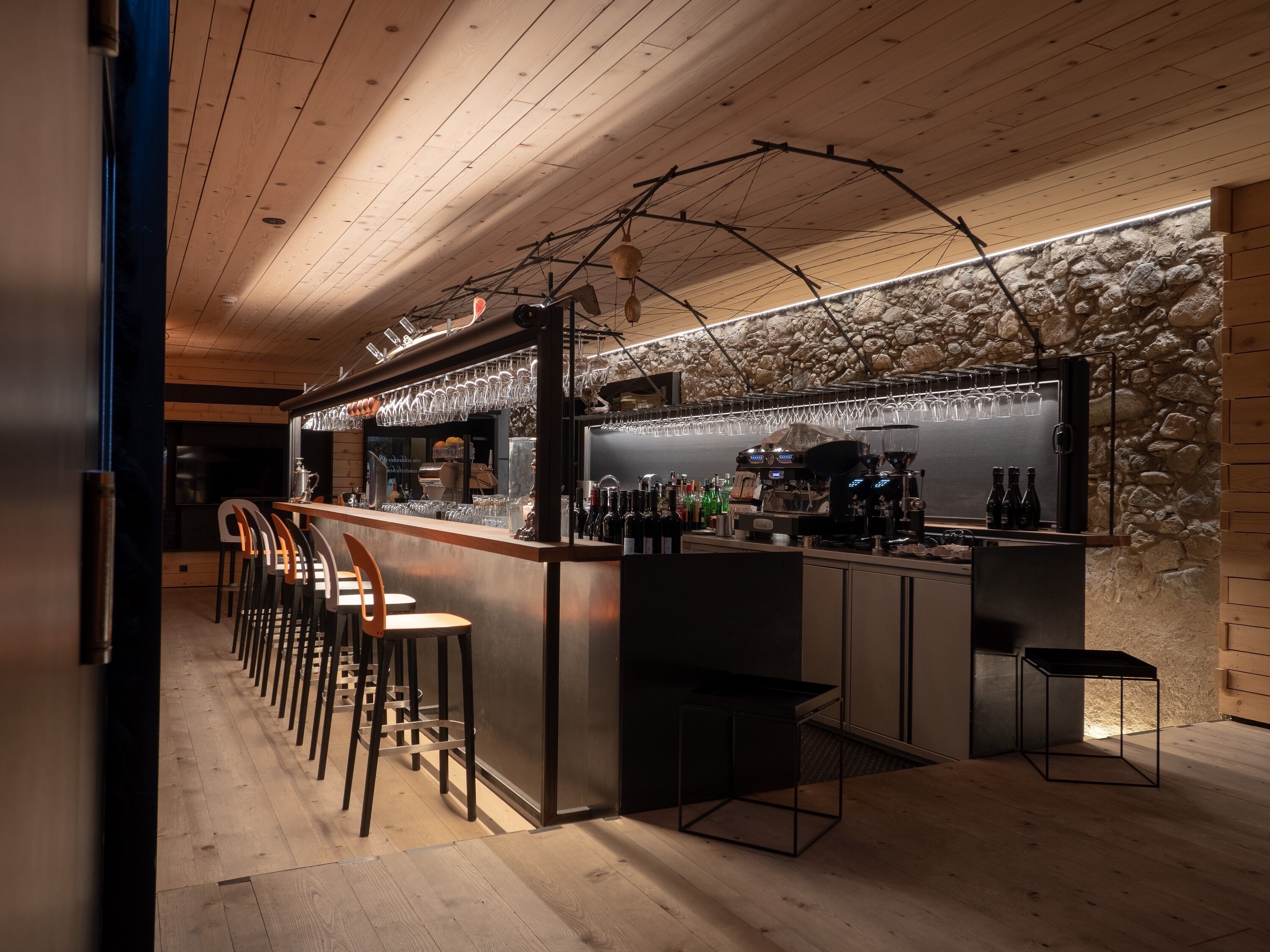 A bar area with wooden ceiling, stone wall, and bar stools.