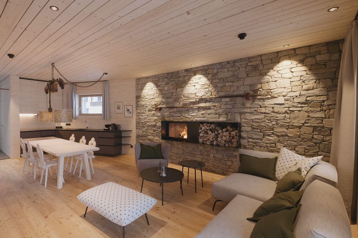 A modern living room with a stone fireplace, wooden ceiling, and a dining area with white furniture.