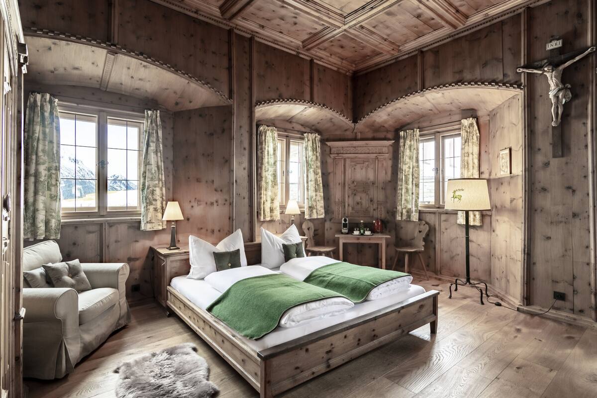 A wooden-paneled bedroom with a bed, a chair, a nightstand, and a lamp.